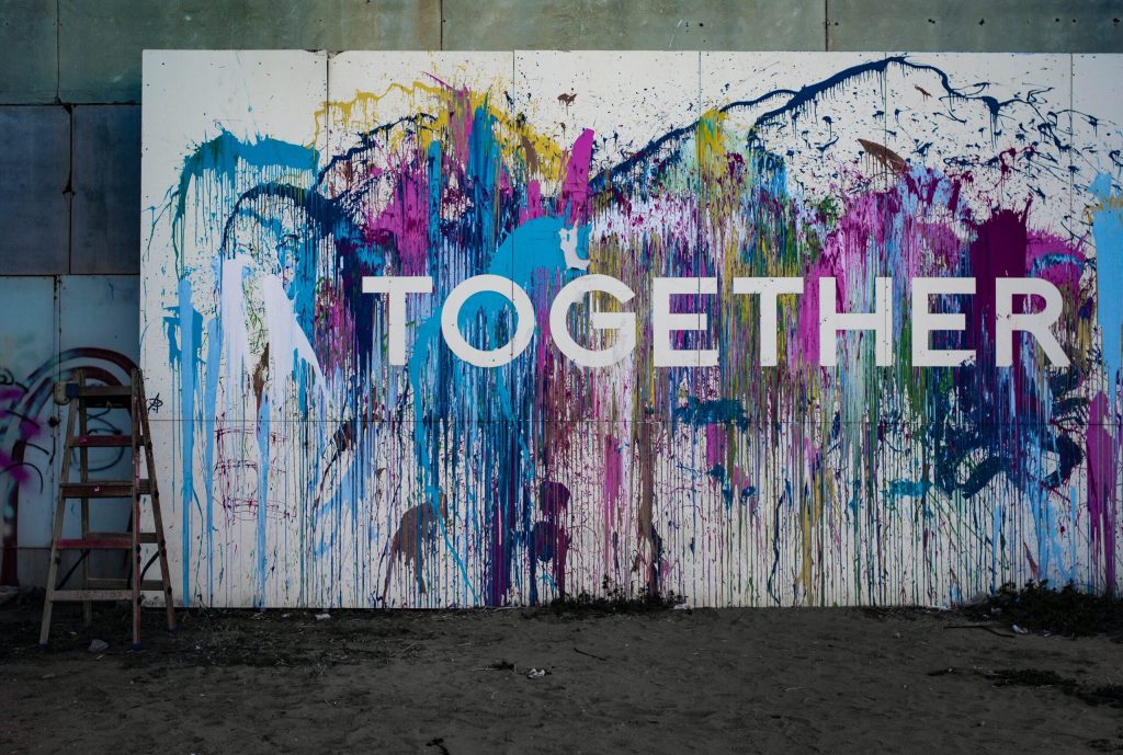 A wall covered in bright paint splatters revealing the word 'Together'