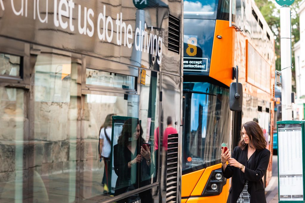 Person stepping onto a bus holding a mobile ohone in their hand.