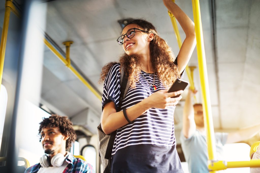 A person smiling on a bus with a phone in their hand.