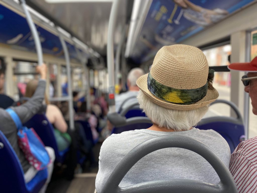 An older, fashionable lady sitting at the back of a busy single decker bus.