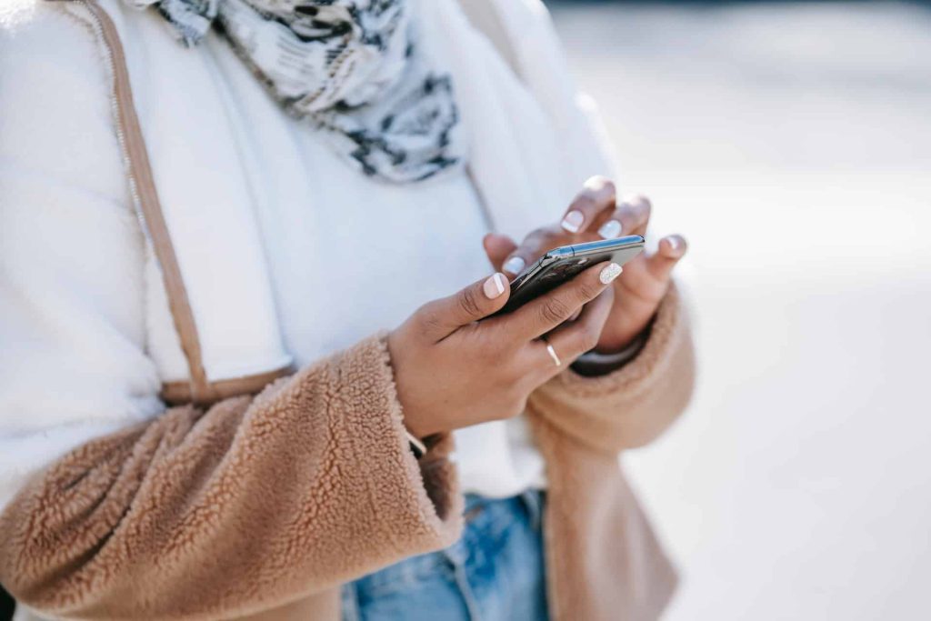 Crop woman in warm jacket using smartphone in street