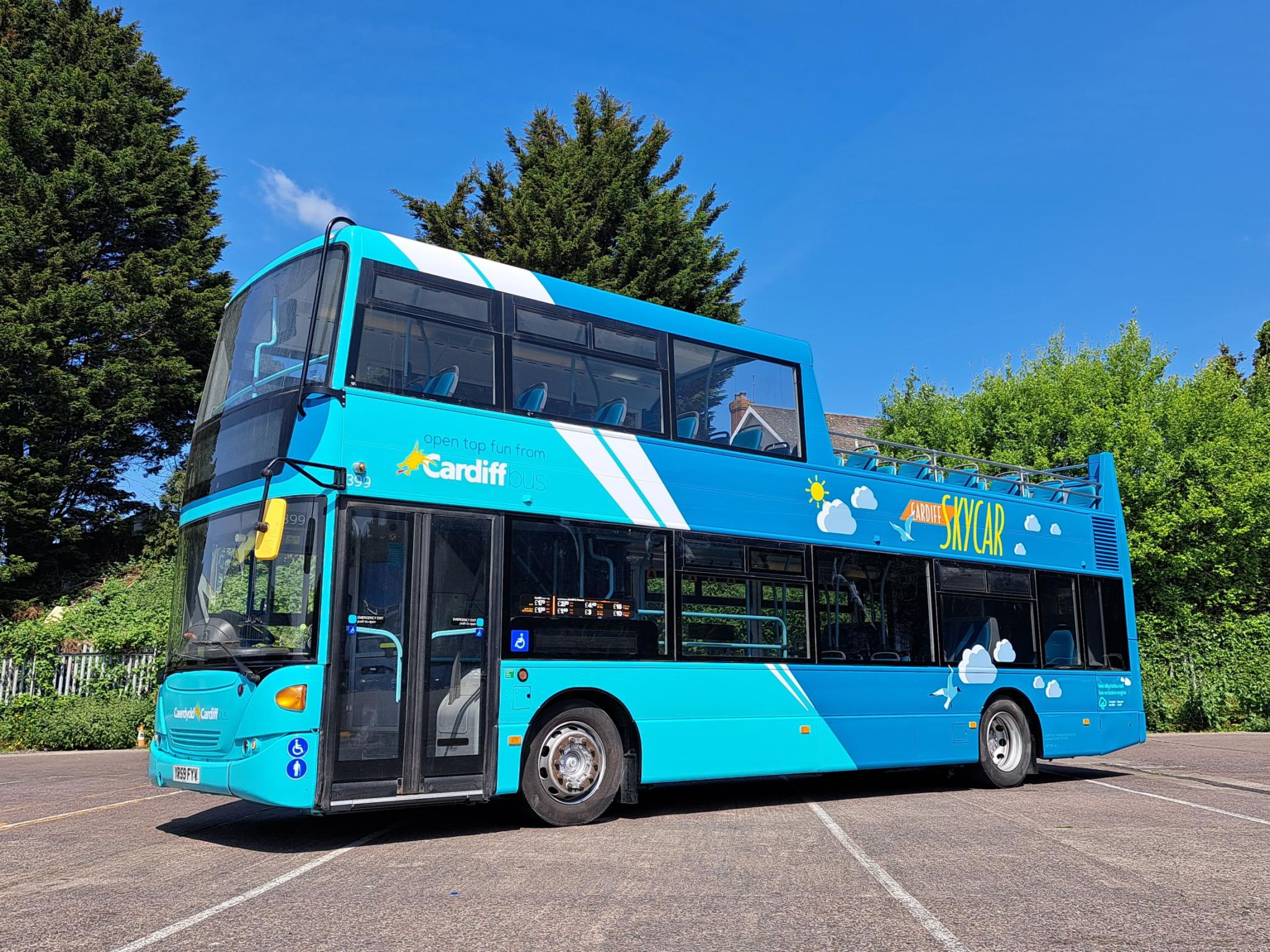 An empty open-top double-decker bus with “Open top fun from Cardiff Bus” written above the entrance door. The words “Cardiff Skycar” are also written on the side towards the back.