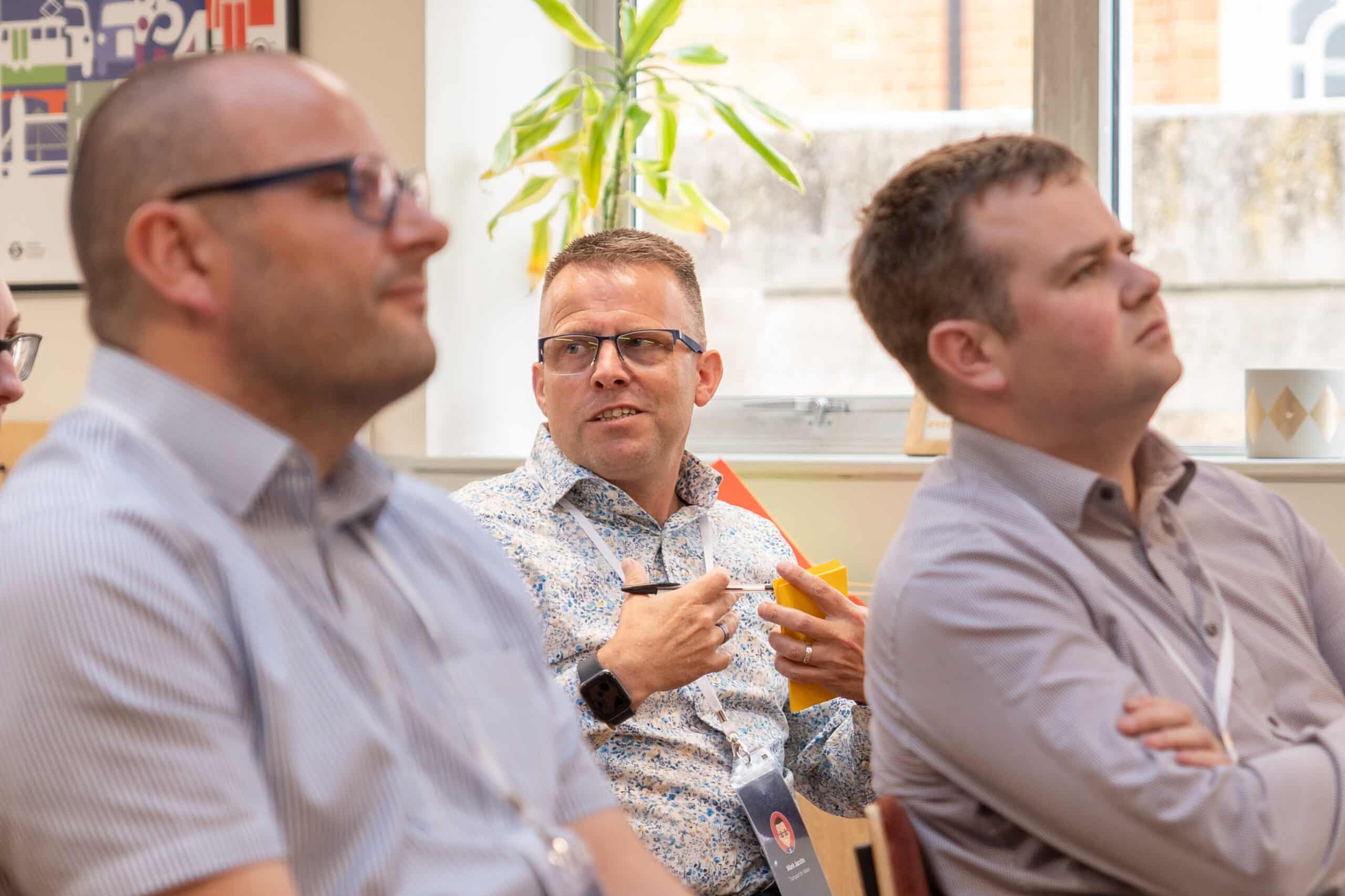 A close up of three men in an audience. One is asking a question.